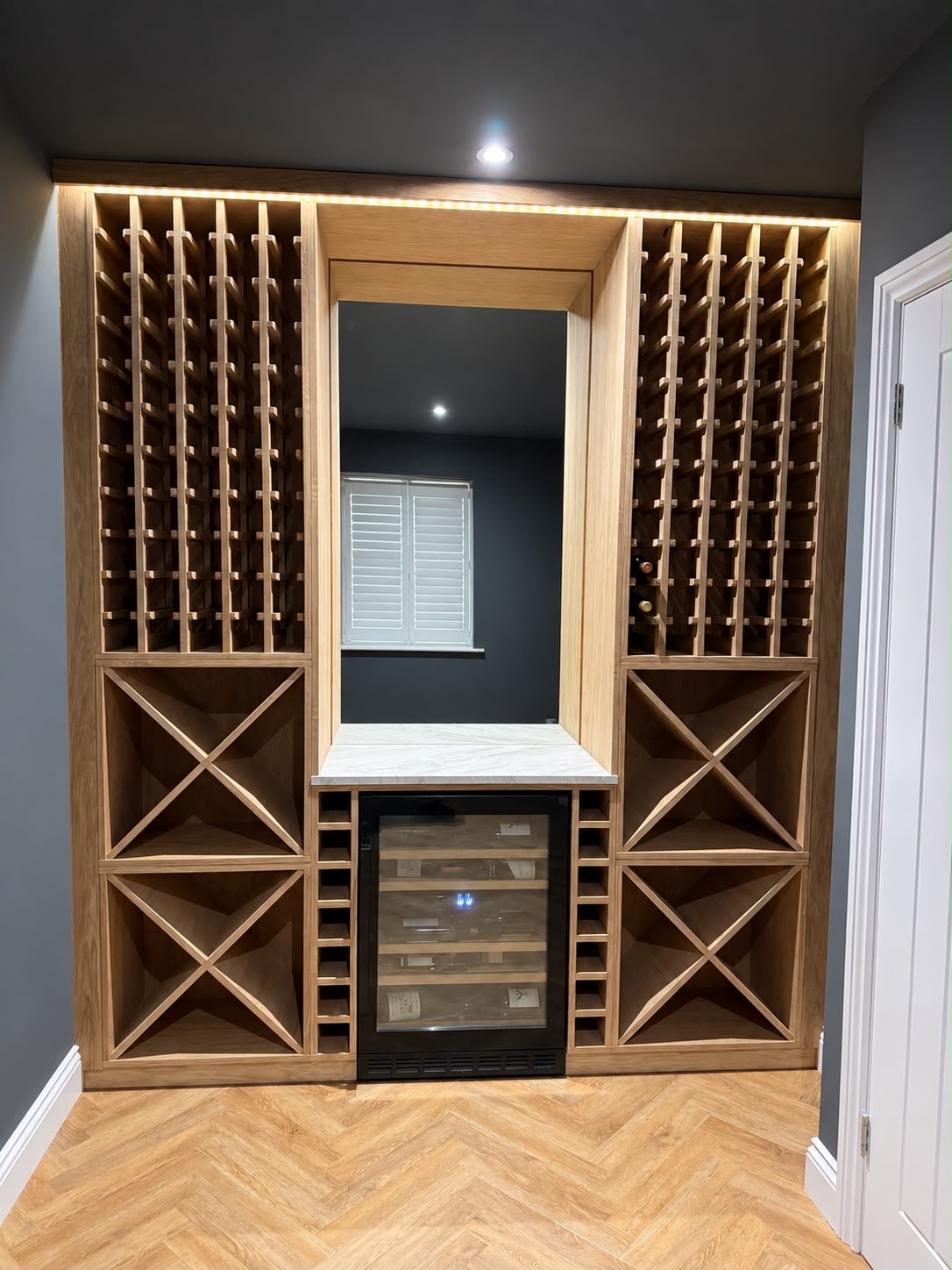 Bespoke oak wine storage wall with ambient lighting, built by Rymax Carpentry and Building